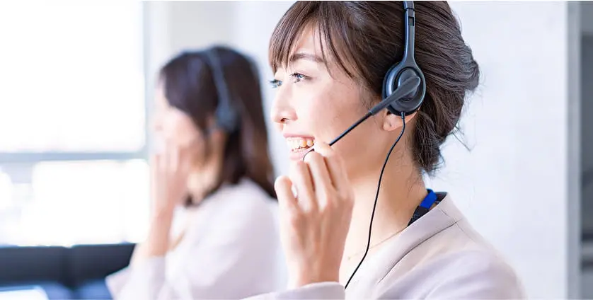 ヘッドセットを着けた女性スタッフが、笑顔で対応しているコールセンターの様子。